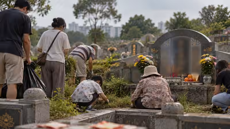 A family tidying their ancestors' grave in Singapore, with flowers, oranges and incense set before the headstone. The inscriptions are blurred.